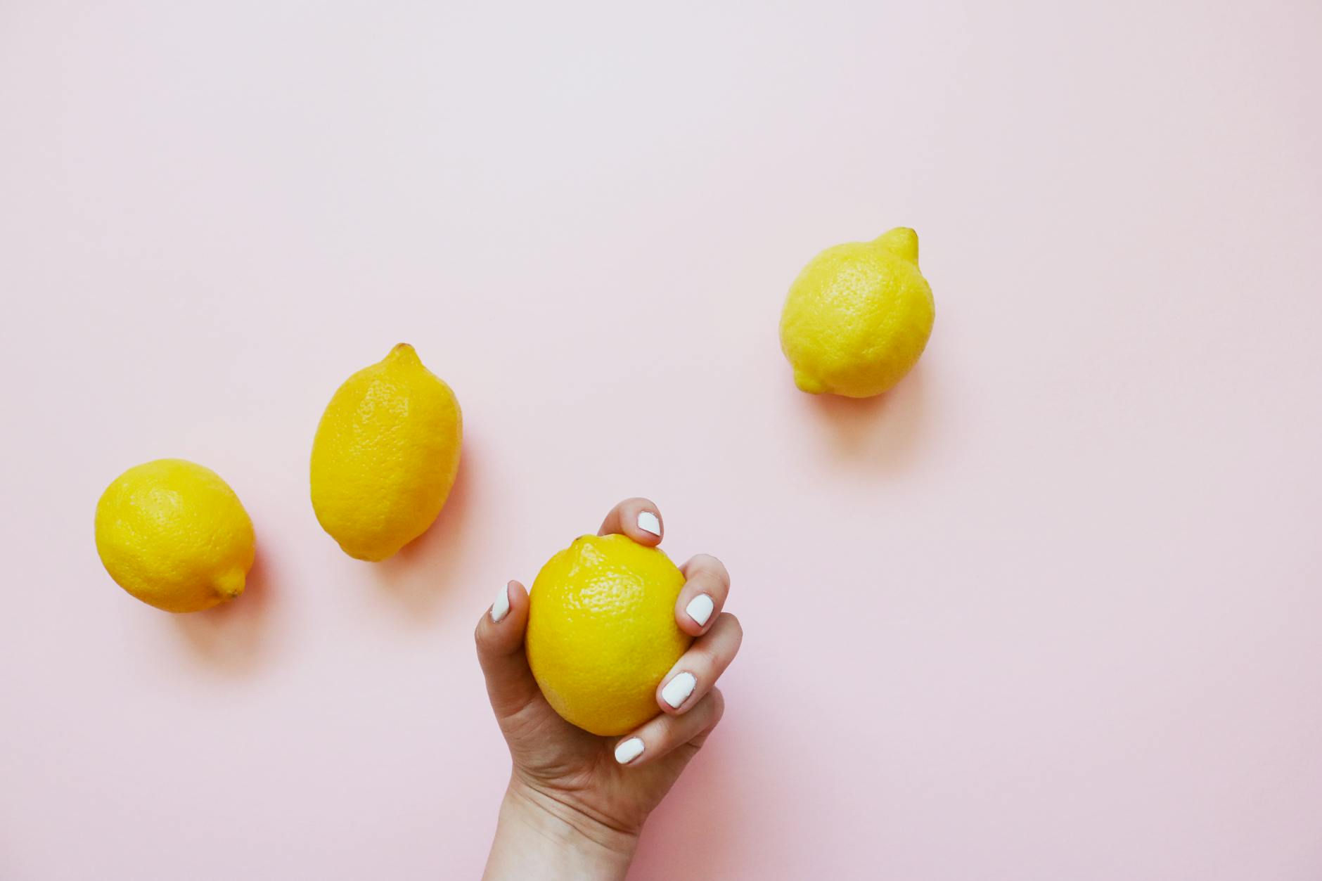 A hand holding a fresh lemon on a soft pink background, evoking natural wellness and refreshing sensation.