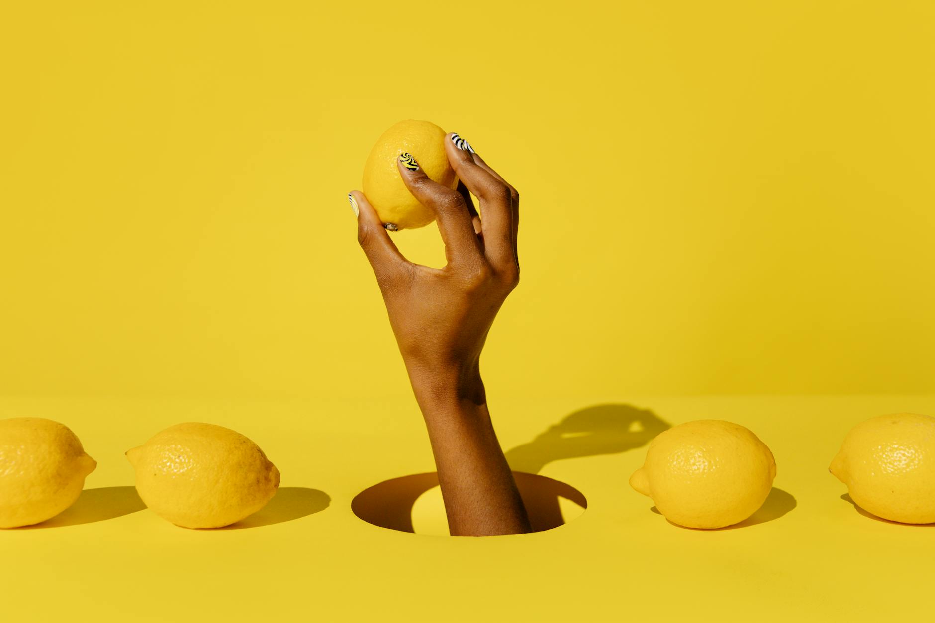 A hand holding a fresh lemon against a bright yellow background, symbolizing the Lemon clitoral vibrator