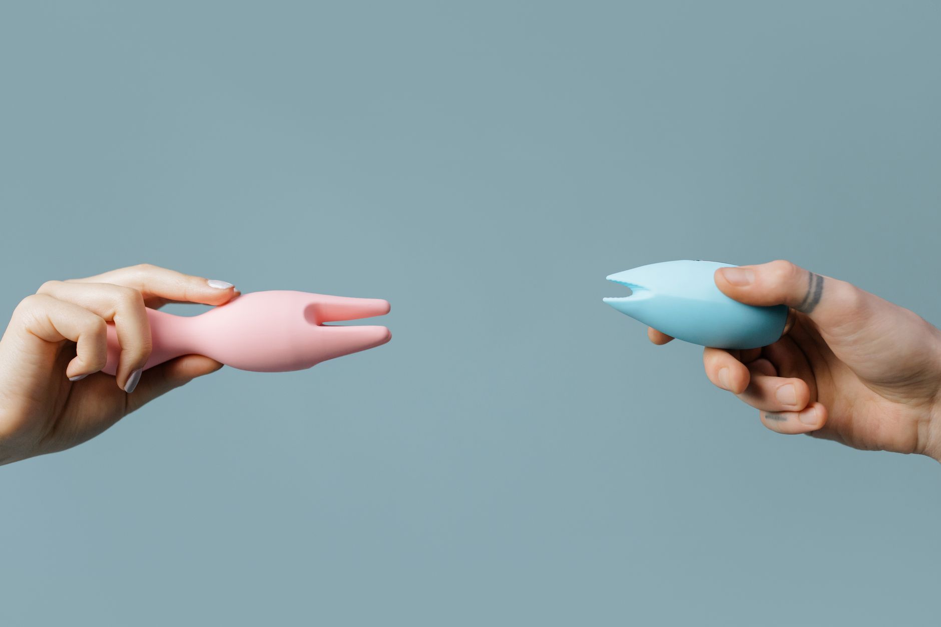 Donna che tiene in mano un vibrator blu e rosa contro uno sfondo pastello