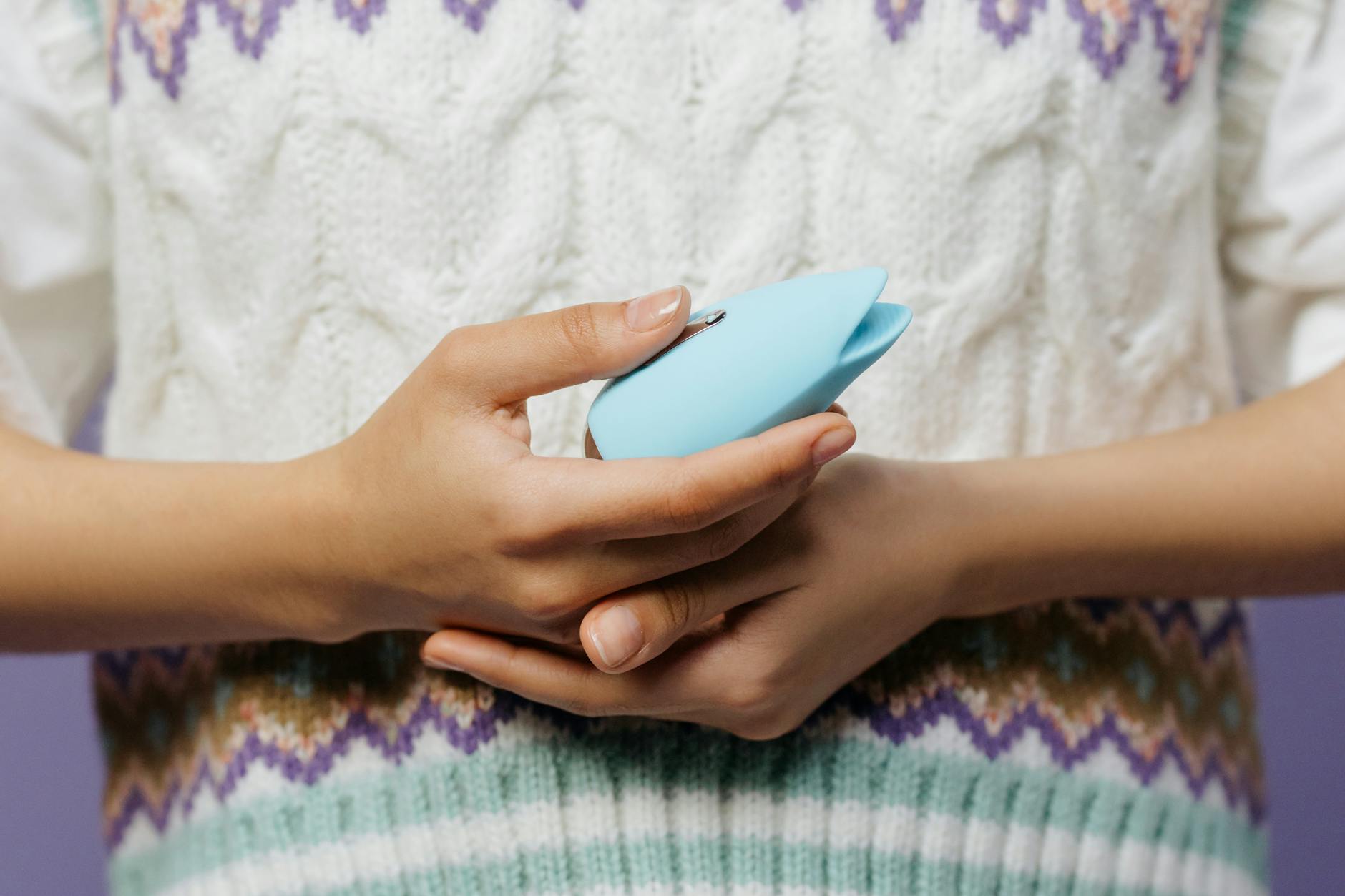 Mani che tengono un massaggiatore personale blu contro un maglione lavorato a maglia