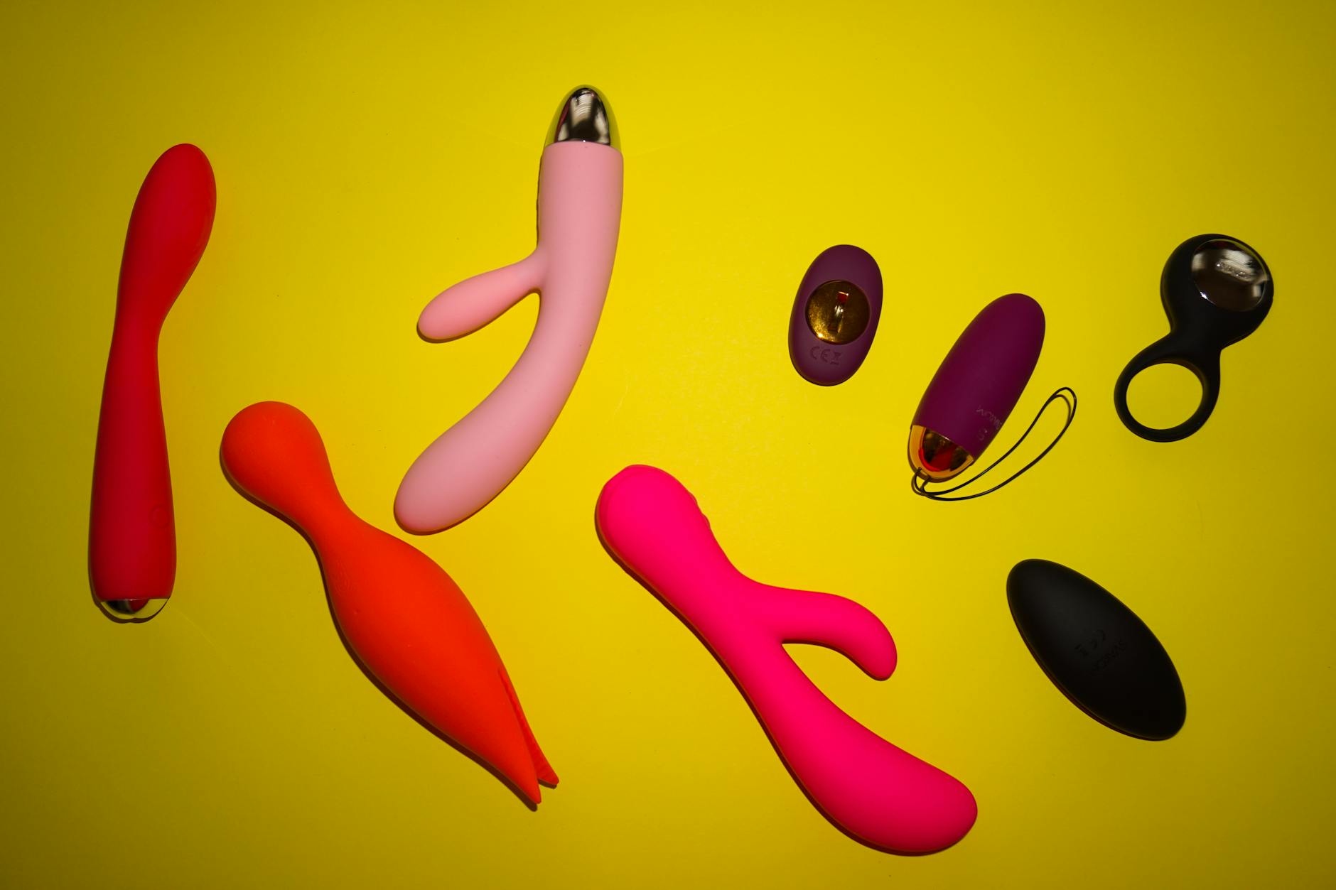 Vibrant collection of various sex toys and clitoral vibrators arranged on a bright yellow surface