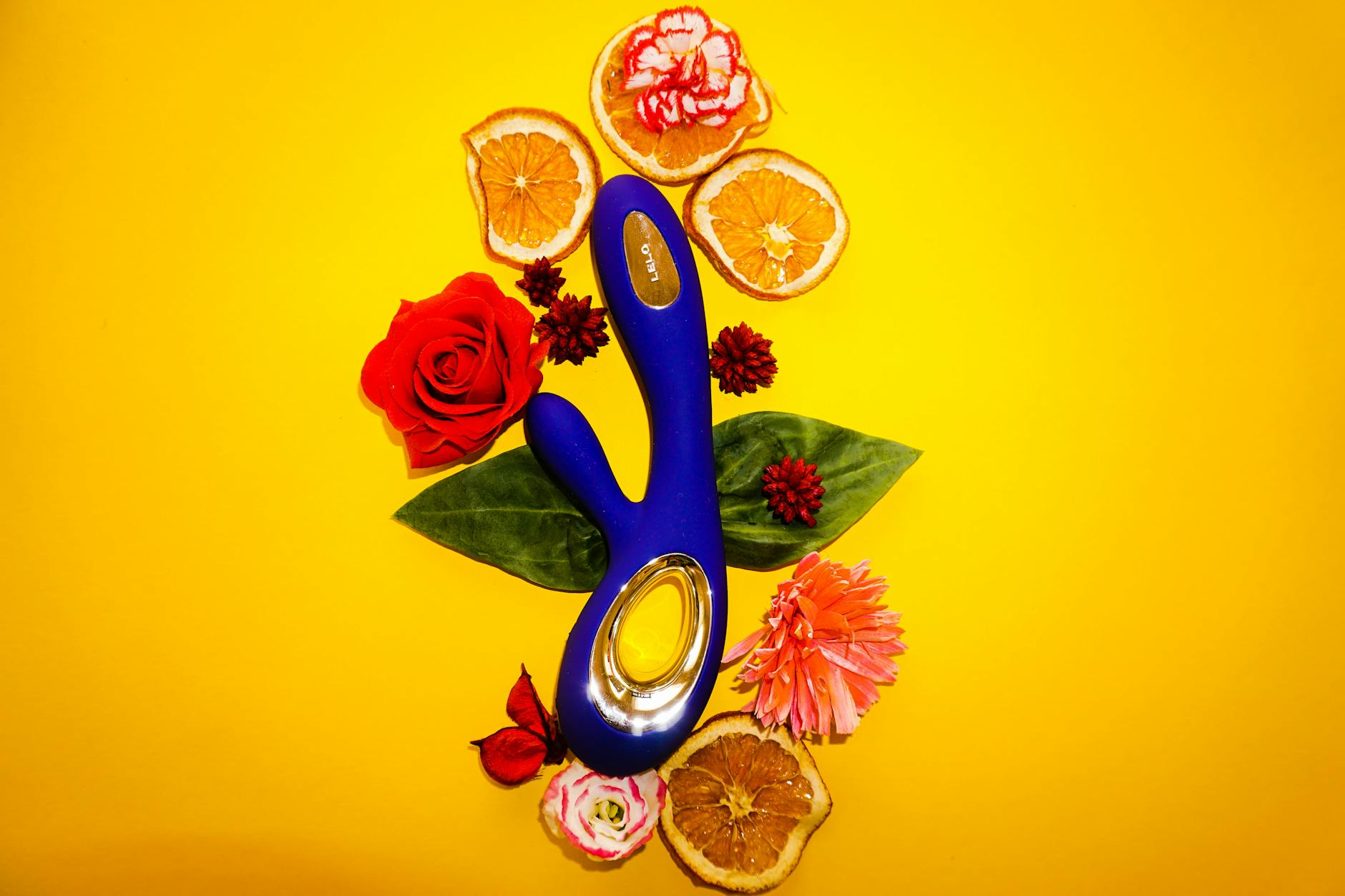 A blue lemon vibrator surrounded by flowers and citrus on a yellow background